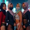 Four women in hijabs and lingerie pose on a city street at night
